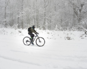 an unknown mountain biker bundles up and braves a january blizzard to get in a winter ride among the forests umstead state park, morrisville north carolina.
