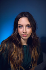 Fototapeta premium portrait of a girl in a green dress sitting on a gray bed against a blue wall