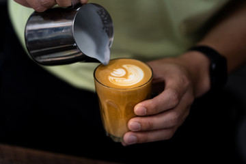 Close-up of male barista hand holding and pouring hot milk for prepare latte art on piccolo latte cup of coffee.