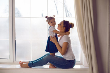 mother and daughter in white t-shirts sitting on the window