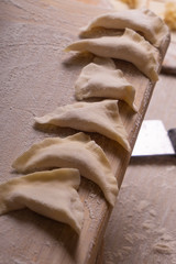 Dumplings, dumplings, ravioli. Plywood cutting board, wooden flour sieve and wooden rolling pin - tools for making dough.