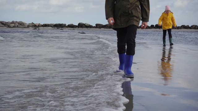 Two children walking along the coast of Baltic sea in rubber boots. Slow motion.
