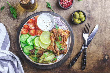 Lunch bowl with grilled chicken, red onion, tomato, cucumber, lemon, olive and sause on wooden background. Top view.