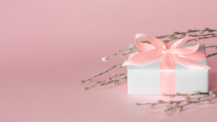 White gift box with pink ribbon and pussy-willow twigs on pastel pink background with copy space. Happy Mother's Day, Women's Day, Valentine's Day or Birthday spring minimalistic greeting card.