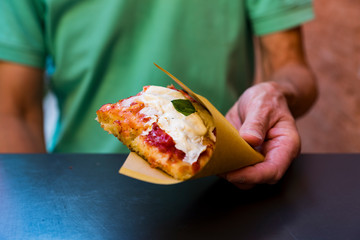 Man holds slice of pizza (or Focacchia) in paper bag
