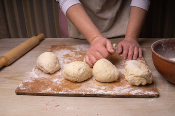 A woman kneads the dough. Plywood cutting board, wooden flour sieve and wooden rolling pin - tools for making dough.
