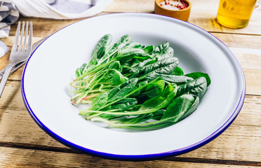 Fresh green baby spinach on plate on wooden rustic table. Healthy diet, vegetarian food concept.