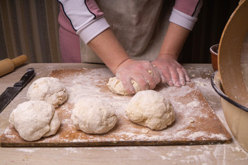 A woman kneads the dough. Plywood cutting board, wooden flour sieve and wooden rolling pin - tools for making dough.