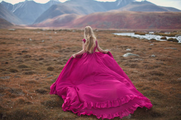 A girl in a pink dress walks on a background of mountains.