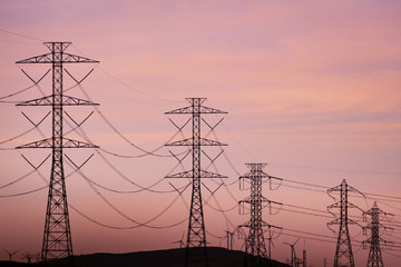 Sunset view of high voltage electricity towers on the hills of San Francisco bay area; Wind turbines visible in the background; California