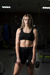 Portrait of a girl with dumbbells in the gym against a dark background.