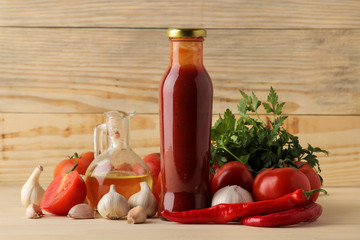 Red sauce in a bottle and ingredients for cooking, butter. tomatoes, peppers, garlic on a natural wooden background