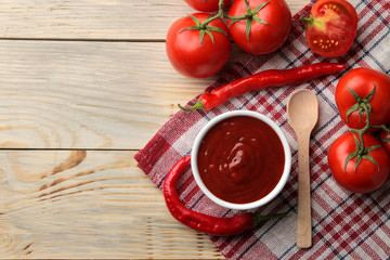 Red sauce or ketchup in a bowl and ingredients for cooking, tomatoes and peppers on a natural wooden background. top view