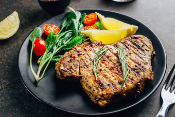 Roasted pork steak on black plate over dark background. With lemon, Cranberry Sauce and wine.