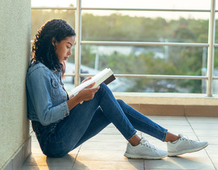 A college girl with Asian features is reading a book sitting on the floor