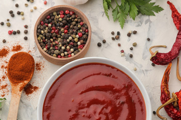 Red sauce or ketchup in a bowl and ingredients for cooking, spices, garlic, pepper and herbs on a light concrete background. top view