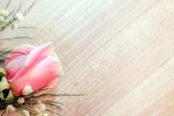 A fresh pink rose flower with white baby's breath (Gypsophila) and greenery against white-washed wood, with copy space