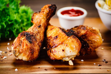 Roast chicken drumsticks with french fries on wooden board