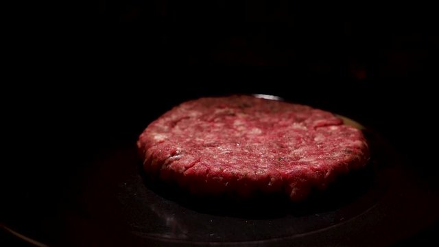 Close up of raw burger beef patty on black background, food and cooking concept. Stock footage. Fresh beef cutlet lying on a frying pan.