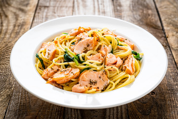 Pasta with salmon and spinach on wooden background