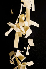 Falling pasta. Flying yellow raw macaroni over black background