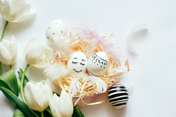 Easter background with easter eggs in the nest, spring flowers and white feathers. Top view with space for copy. White tulips