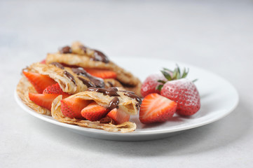 Pancakes with strawberries and chocolate sauce.  Strawberries sprinkled with powdered sugar.  Close-up.  Light background.
