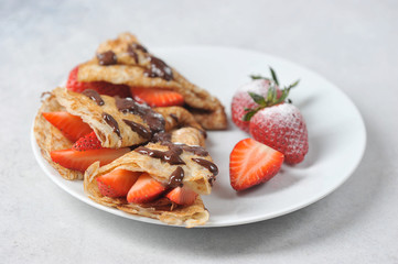 Pancakes with strawberries and chocolate sauce.  Strawberries sprinkled with powdered sugar.  Close-up.  Light background.
