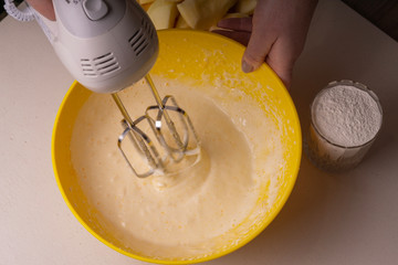 A woman mixes the ingredients for a pie in a yellow bowl with an electric mixer.