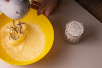 A woman mixes the ingredients for a pie in a yellow bowl with an electric mixer.