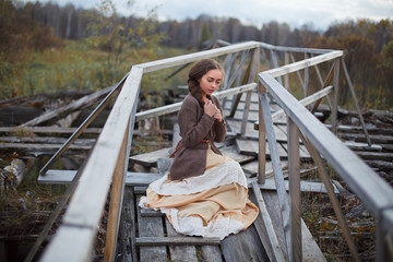 girl in vintage dress stands on a bridge