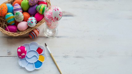 Top view, multicolor and different designs in straw basket next to palett filled with paint color. Copy space on white wooden surface.