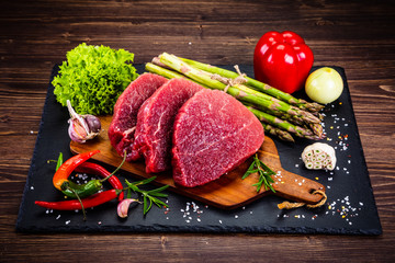 Fresh raw beef steaks on cutting board and vegetables