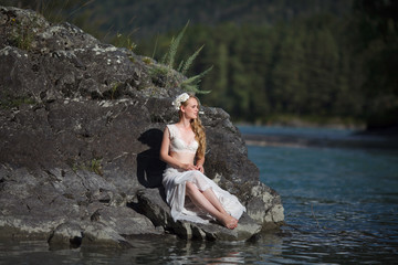  A girl in white clothes stands on a rocky shore near the river.