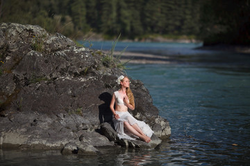  A girl in white clothes stands on a rocky shore near the river.