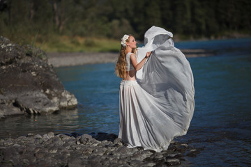  A girl in white clothes stands on a rocky shore near the river.