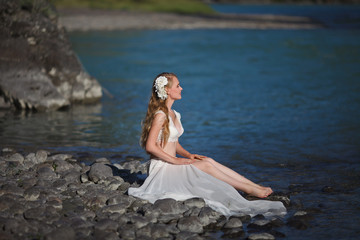  A girl in white clothes stands on a rocky shore near the river.