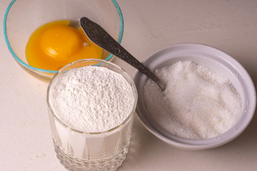 Ingredients for homemade pie stand on the table. Flour, sugar and egg. Close-up.