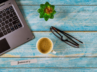 Office table with January month of calendar year, computer and coffee cup, glasses view