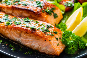 Fried salmon steaks with vegetables on wooden table