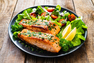 Fried salmon steaks with vegetables on wooden table