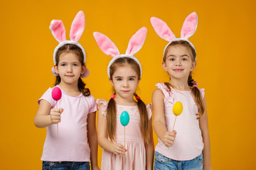 happy cute little child girls with pink bunny ears holding painted Easter eggs on studio yellow background. Easter day