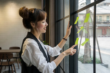 Asian creative business female thinking with note and sticking at contact sheet on glass wall in office.