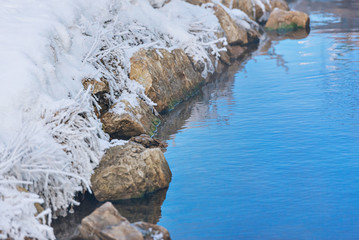 the shore is covered in frost on a frosty day. unfrozen water and snow on rocks