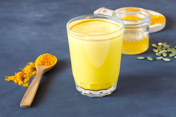 Healthy golden milk with turmeric and honey on a gray background and tiextile. Diet, vegan and detox hot drink. Trendy drink. Copy space. Flat lay.