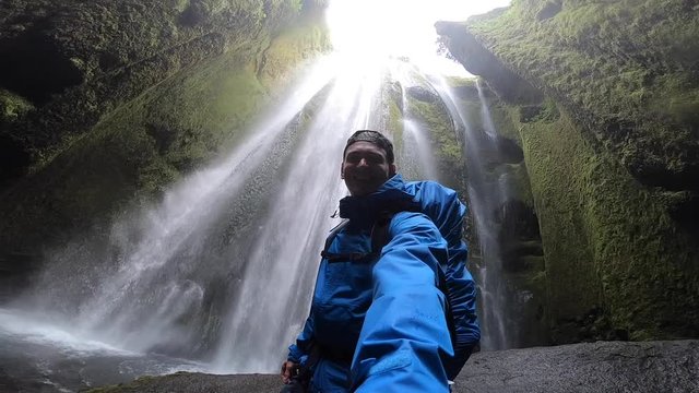 Backpacker exploring the famous touristic powerful waterfall Gljufrabui in the cave, slow motion, Iceland