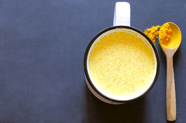 Healthy golden milk with turmeric and honey on a gray background and tiextile. Diet, vegan and detox hot drink. Trendy drink. Copy space. Flat lay.