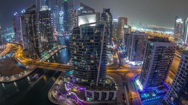 Panoramic aerial view of Dubai Marina residential and office skyscrapers with waterfront night timelapse with traffic on a bridge. Floating boats and yachts
