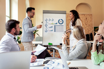 Group of young business people working together in office, two coworker conducting a business presentation using flip chart.