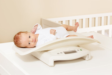 Little baby boy lay on the scale for measuring body weight and looking at camera